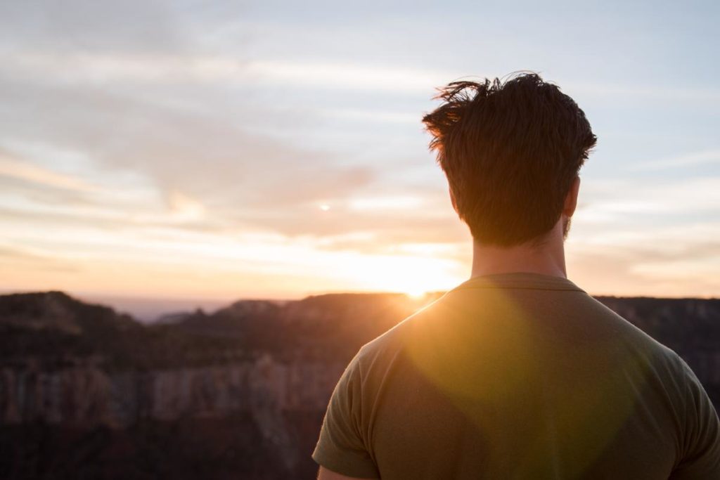 Man stares at mountain after hike, relishing in benefits of detox