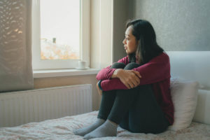 a person looks sadly out of a window possibly considering a Dual diagnosis programs in San Diego