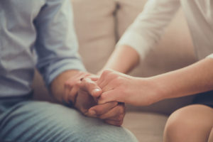 two people hold hands on a couch in a close up of their hands as they deal with alcohol dependency