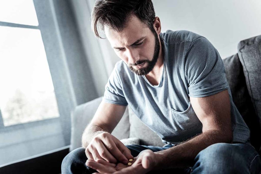 a person sits on a couch and counts out pills while experiencing signs of prescription drug dependence