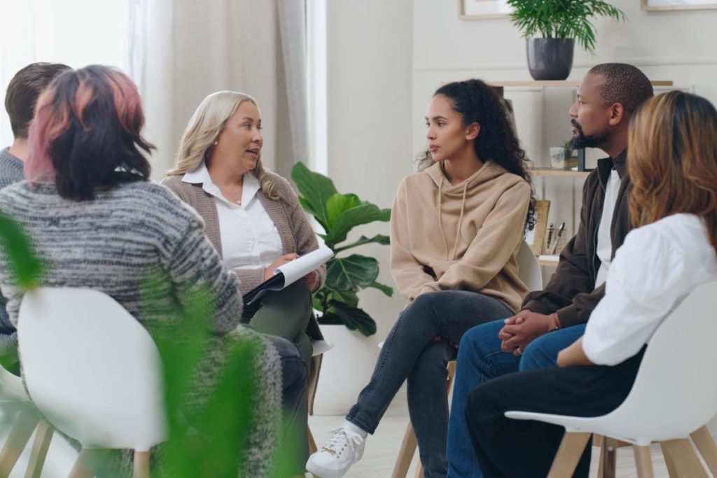 a group of people sit in chairs in a circle and participate in intensive outpatient therapy