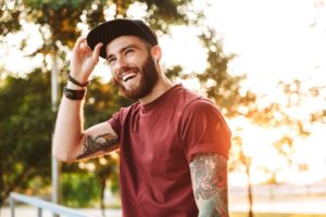 a person with a beard in a hat stands outside and smiles after learning what is dual diagnosis treatment
